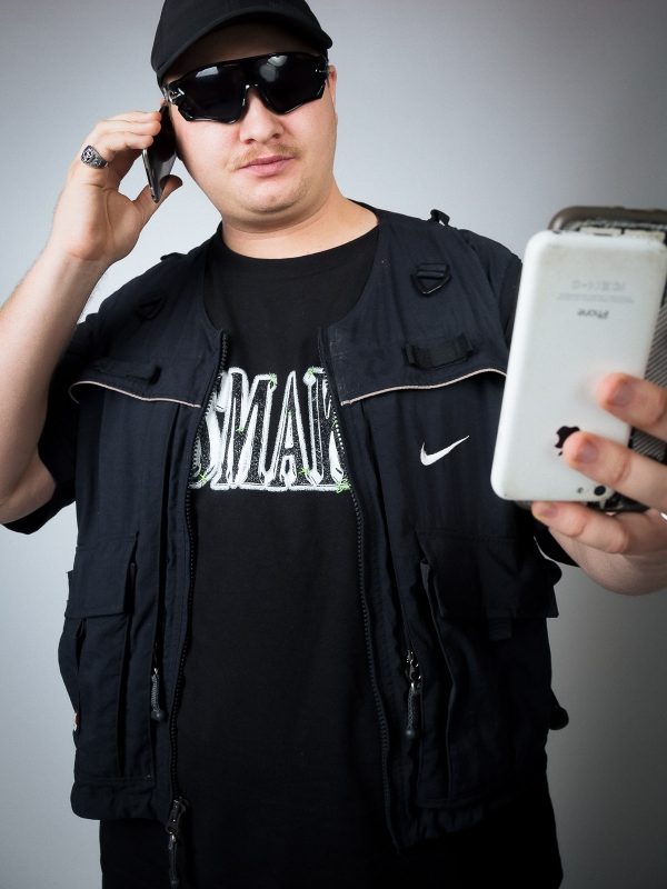A man holds a phone while modelling Smak (Rapper) merch